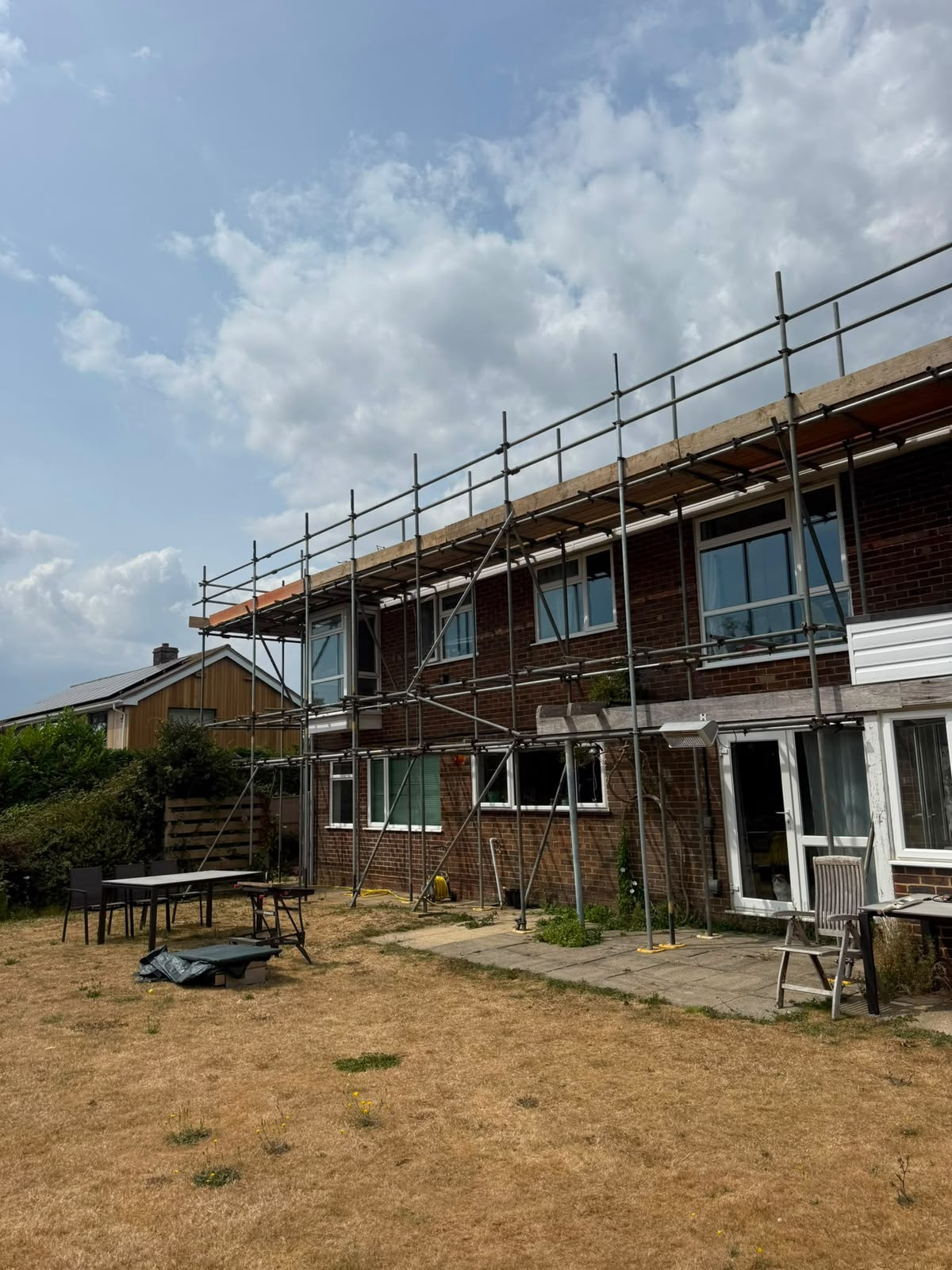 Scaffold frame at roof level along a house, ready to carry a temporary roof