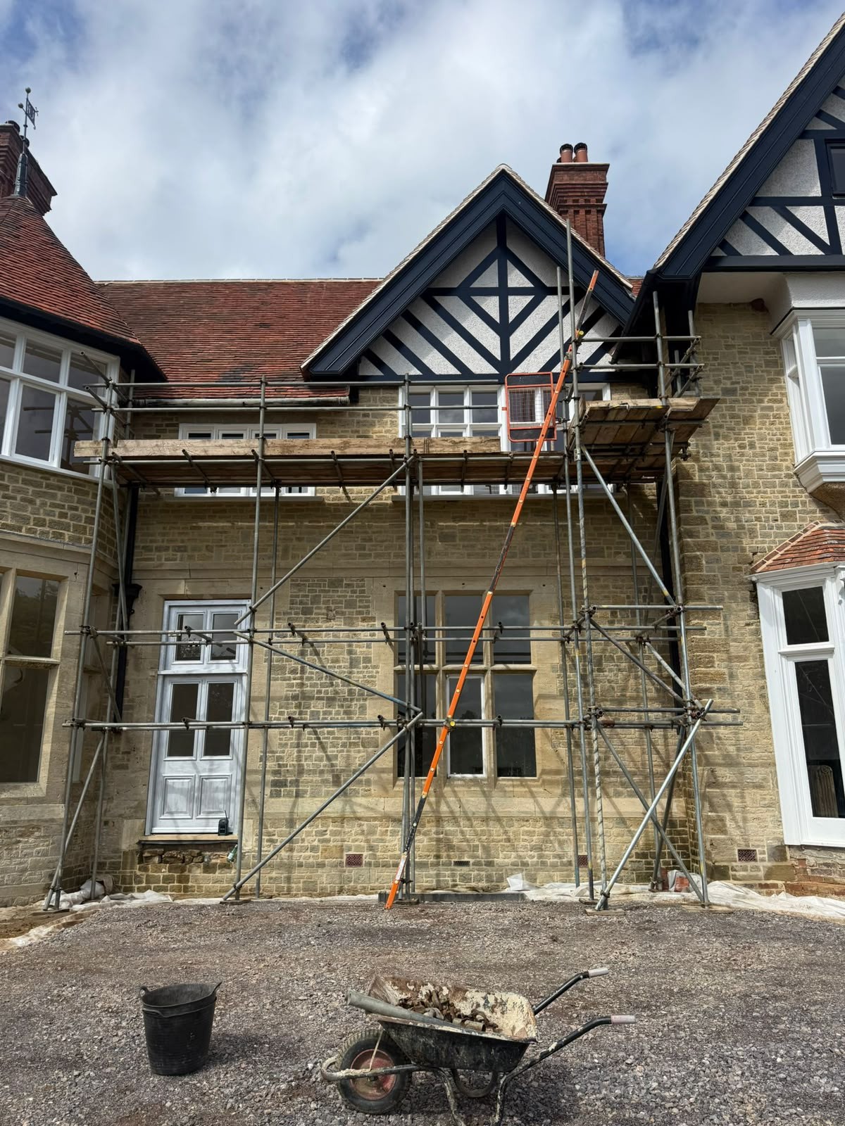 Tube and fitting scaffold with boarded lift erected across a stone-built house for roof and window works