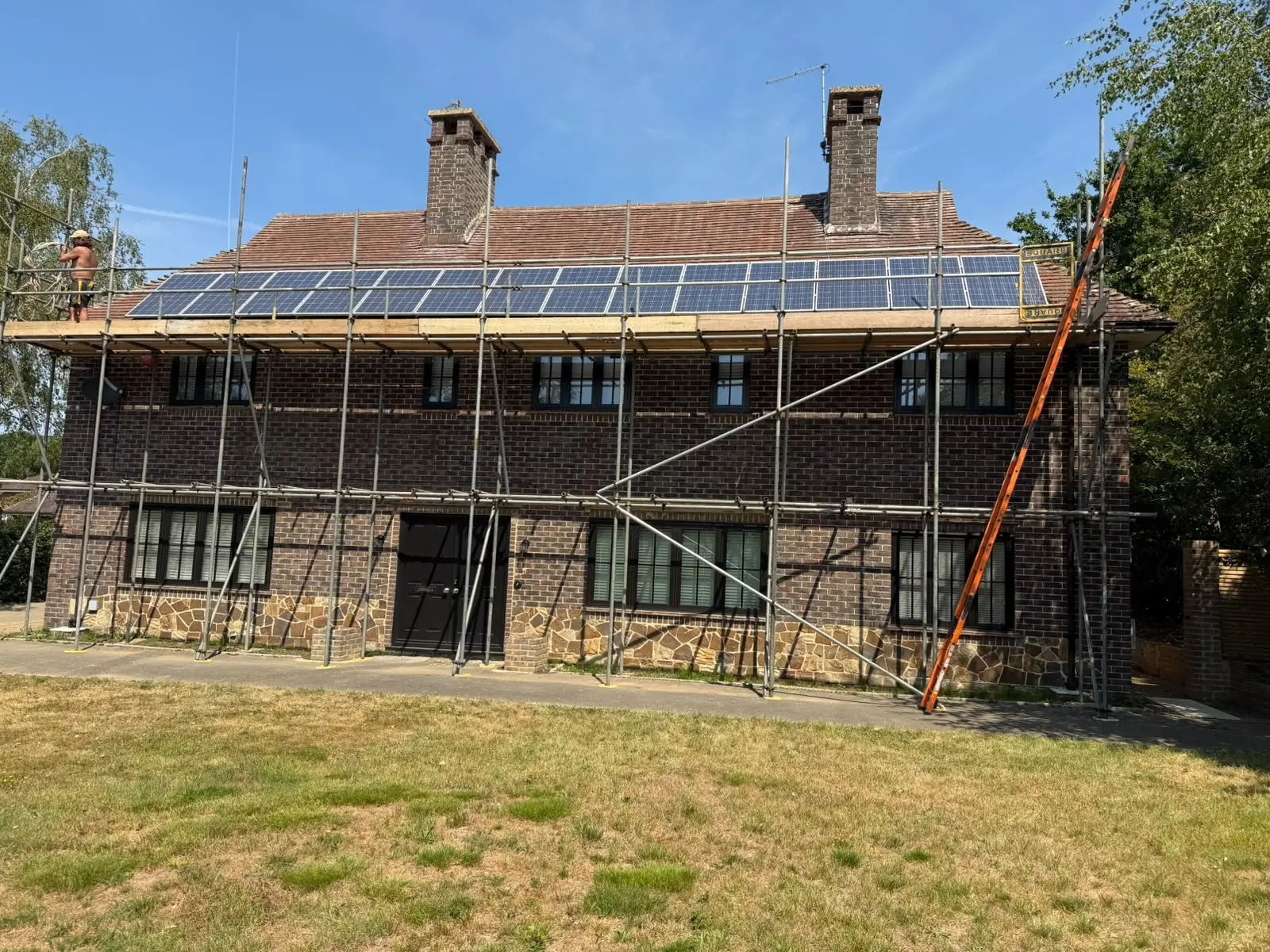 Scaffolding erected across the full width of a large brick house during solar panel installation