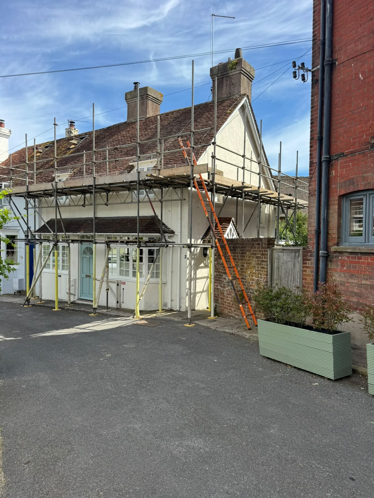 Scaffolding to a village cottage roof with pavement-level standards and ladder access