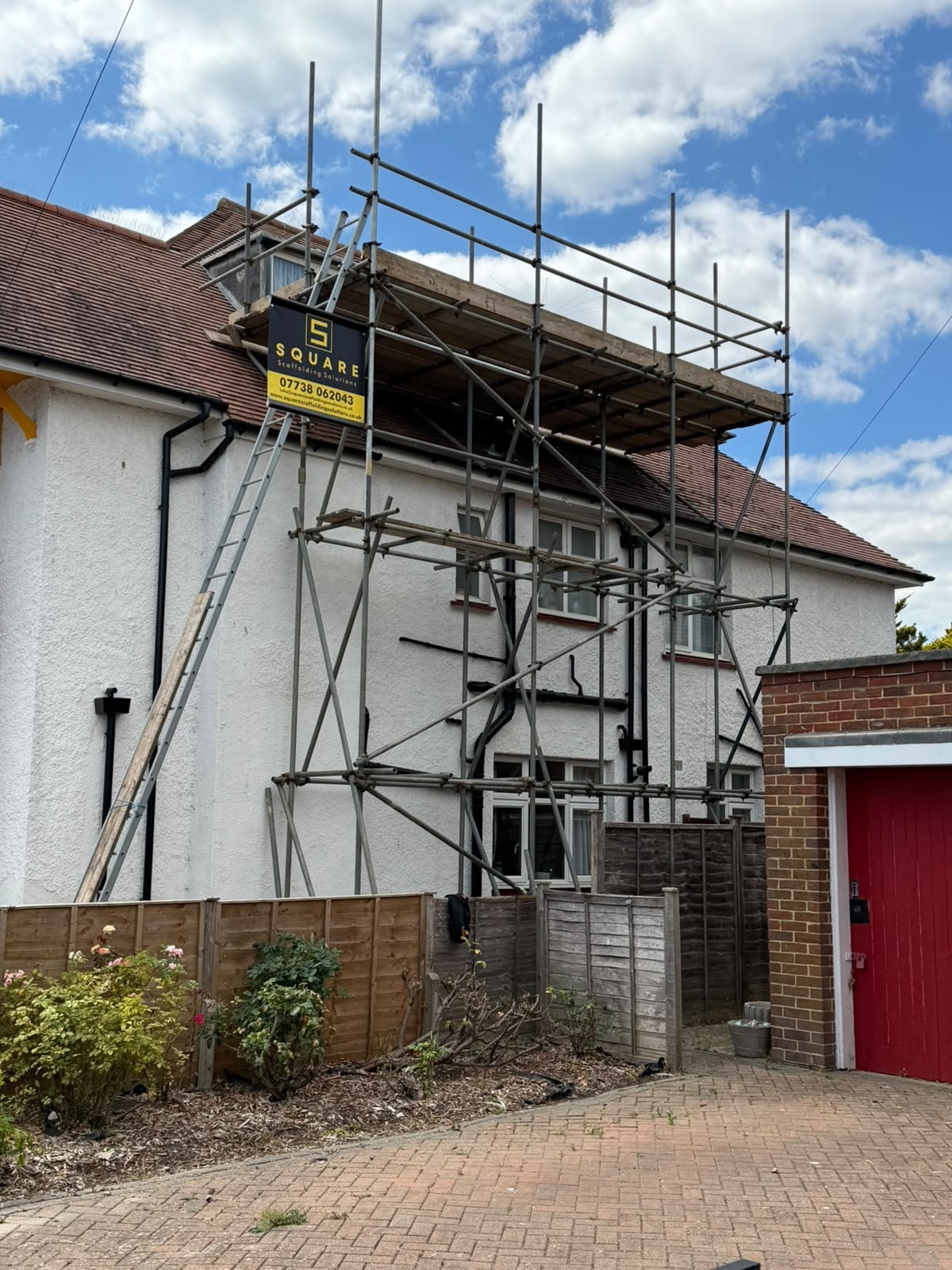 Hired scaffold with boarded lifts and ladder access to the side of a rendered house